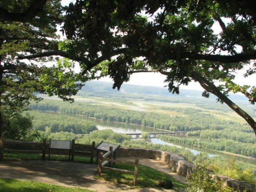 Scenic view from a lookout point, featuring a river winding through lush green landscapes and trees in the foreground.