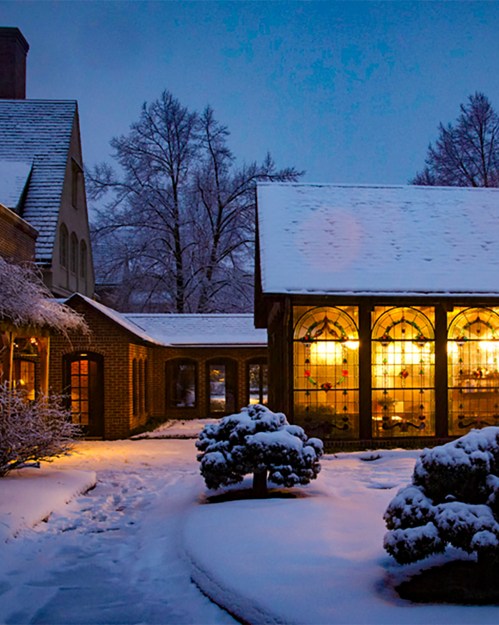 A cozy building illuminated at dusk, surrounded by snow-covered trees and a snowy landscape.