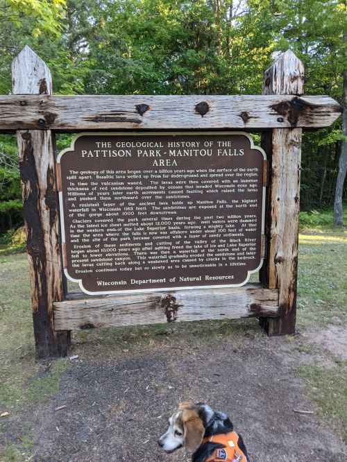 Sign detailing the geological history of Pattison Park-Manitou Falls Area, with a dog in the foreground.