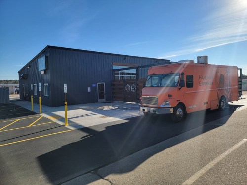 A food truck parked in front of a modern building on a sunny day, with clear blue skies above.