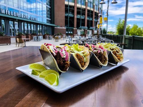 A platter of tacos with various fillings, garnished with colorful toppings, served with lime wedges, outside a cafe.