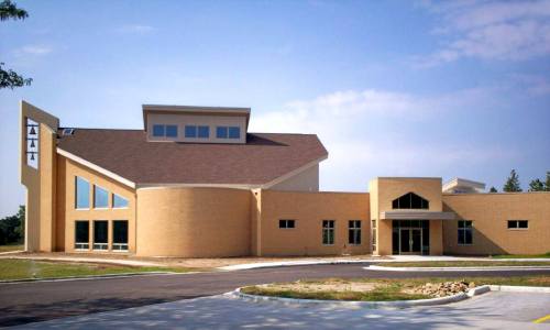 A modern, light-colored building with large windows and a unique architectural design, set against a clear sky.
