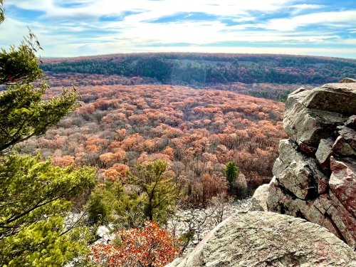 A scenic view of a forested valley with autumn foliage, framed by rocky outcrops and a clear blue sky.