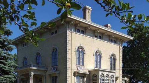 A historic mansion with ornate architecture, large windows, and a lush green surrounding landscape.