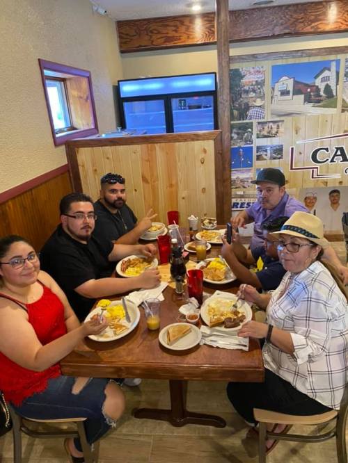 A group of six people enjoying a meal at a restaurant, smiling and holding their plates with food.