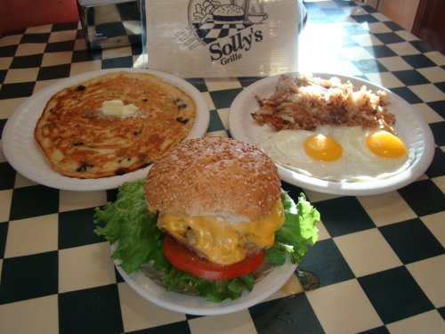 A plate with a cheeseburger, lettuce, tomato, hash browns, and two eggs, alongside a pancake with butter.