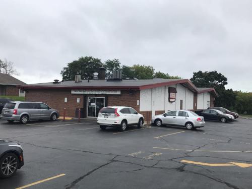 A brick building with a red roof, surrounded by parked cars in a cloudy parking lot.