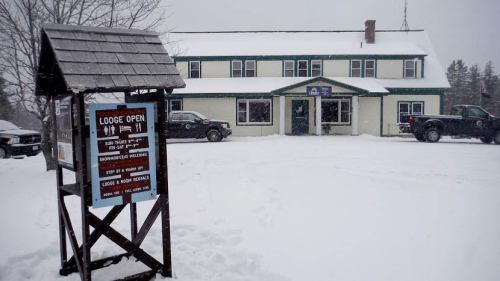 A snowy lodge with a sign indicating it's open, surrounded by parked trucks and a winter landscape.