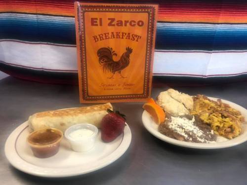 A plate of breakfast with a burrito, eggs, beans, and fruit, alongside a menu for El Zarco restaurant.