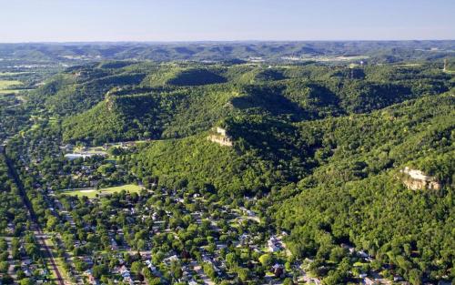 Aerial view of lush green hills and a small town nestled in a valley, surrounded by rolling landscapes.