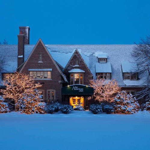 A charming brick house adorned with holiday lights, surrounded by snow, under a twilight sky.