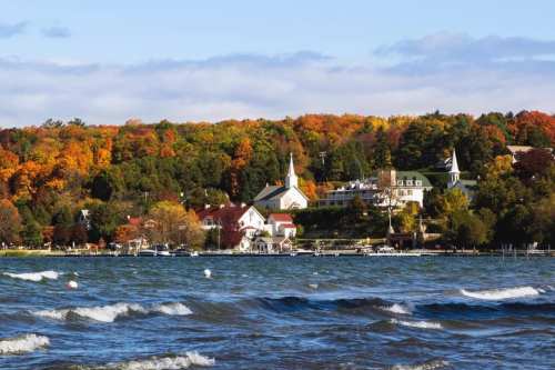 A scenic view of a lake with waves, surrounded by colorful autumn trees and charming buildings along the shore.