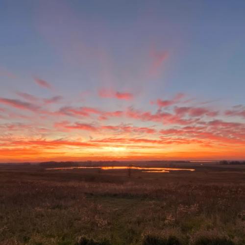 A vibrant sunset over a grassy field, with colorful clouds reflecting in a calm pond.