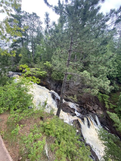 A rushing waterfall flows through a rocky landscape, surrounded by lush green trees and foliage.