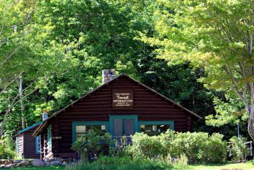 A rustic log cabin surrounded by greenery, featuring a sign that reads "Visitor Information."