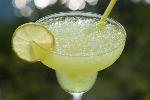 A refreshing green margarita in a glass, garnished with a lime slice and a straw, set against a blurred background.