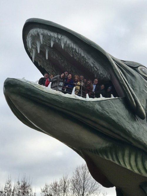 A group of people stands inside the open mouth of a large, frozen fish sculpture, surrounded by winter scenery.
