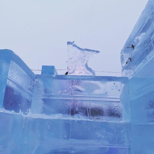 A close-up of a clear ice structure with jagged edges, set against a pale sky.