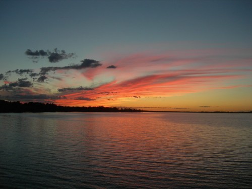 A serene sunset over a calm lake, with vibrant pink and orange clouds reflecting on the water's surface.