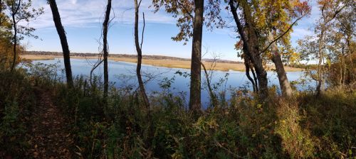 A serene view of a lake surrounded by trees and autumn foliage under a clear blue sky.