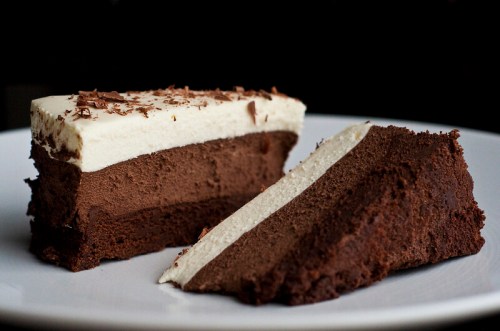 A slice of layered chocolate cake with creamy frosting and chocolate shavings on top, served on a white plate.