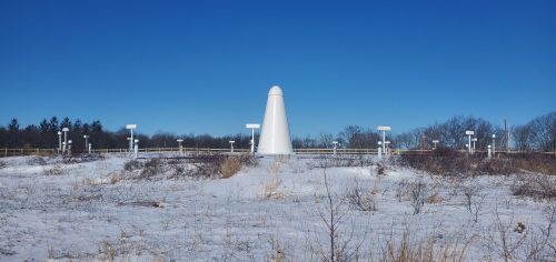 A white conical structure surrounded by snow and a clear blue sky, with various sensors and equipment nearby.