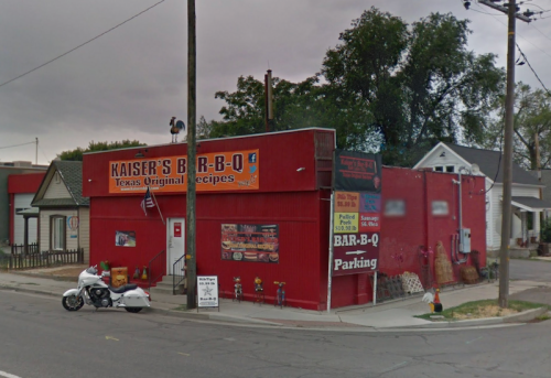 A red building with a sign for "Kaiser’s Bar-B-Q" featuring Texas recipes, with a motorcycle parked outside.