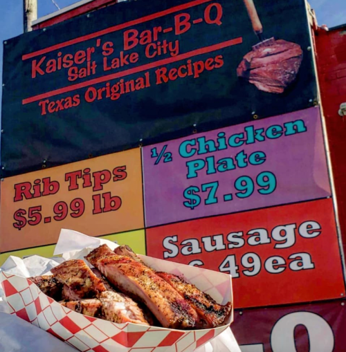 A sign for Kaiser’s Bar-B-Q in Salt Lake City displays menu items and prices, featuring rib tips, chicken plate, and sausage.