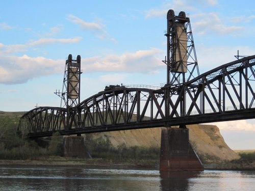 A large, metal lift bridge spans a river, with towers on either side and a scenic landscape in the background.
