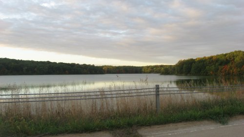 A serene lake surrounded by trees, with a cloudy sky reflecting on the water's surface.
