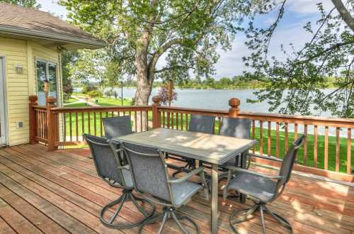 A wooden deck with a table and chairs overlooking a serene lake and lush greenery.