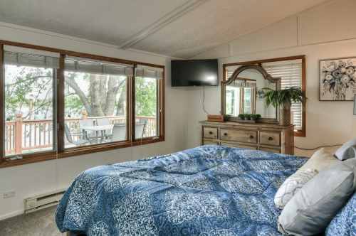 Cozy bedroom with a blue patterned bedspread, large windows, a TV, and a wooden dresser.
