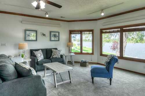 Cozy living room with gray sofas, a blue chair, and large windows overlooking a lake. Bright and inviting atmosphere.