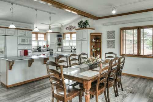 A bright kitchen and dining area featuring a wooden table, chairs, and modern appliances with natural light from windows.