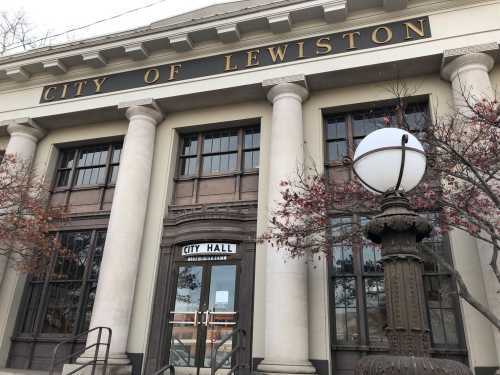 Exterior view of Lewiston City Hall, featuring large columns and a decorative lamp post in front.