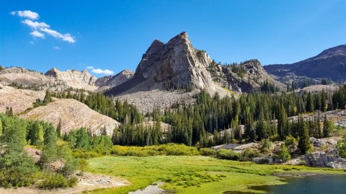 A scenic view of rugged mountains and lush green trees surrounding a tranquil lake under a clear blue sky.