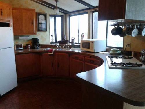 A cozy kitchen with wooden cabinets, a gas stove, microwave, and large windows letting in natural light.