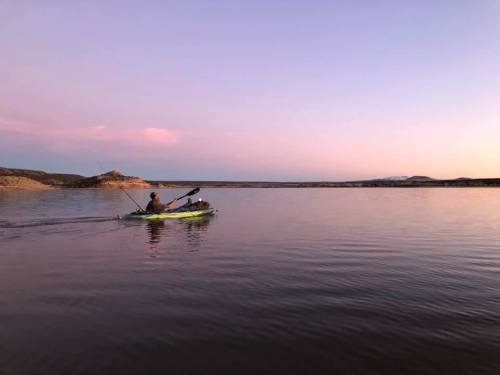 A person kayaking on calm water during sunset, with soft pink and purple hues in the sky.