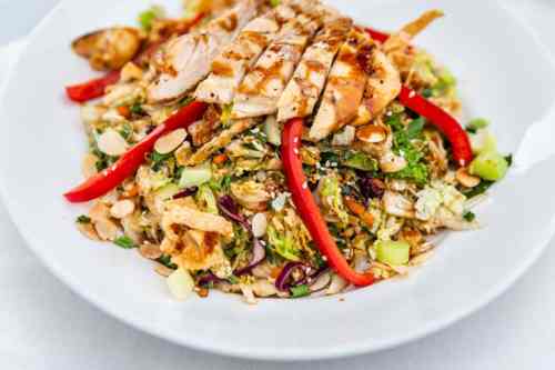 A colorful salad topped with grilled chicken, red peppers, and sliced almonds, served in a white bowl.