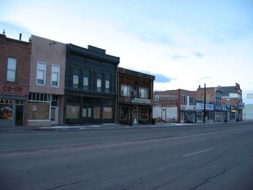 A quiet street lined with historic buildings, some vacant, under a blue sky at dusk.