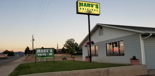 A roadside view of Marv's Drive-In, featuring a sign and a building with a neon open sign at dusk.