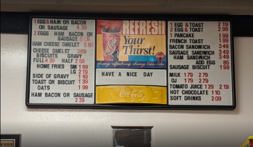 Menu board featuring breakfast items and prices, including eggs, pancakes, sandwiches, and drinks.