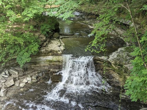 A serene waterfall cascades over rocks, surrounded by lush green foliage in a tranquil forest setting.