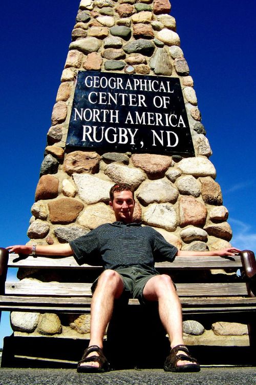 A person sits on a bench in front of a stone monument marking the geographical center of North America in Rugby, ND.
