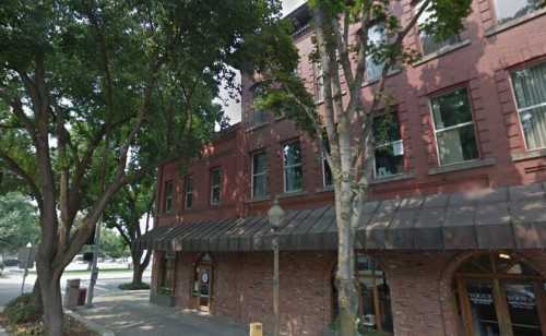 A brick building with large windows, surrounded by trees, featuring a canopy over the entrance.