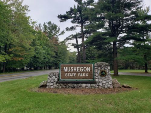 Sign for Muskegon State Park surrounded by trees and grass, indicating the entrance to the park.