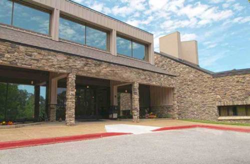 A modern building with stone exterior and large windows, featuring a landscaped entrance and clear blue sky.