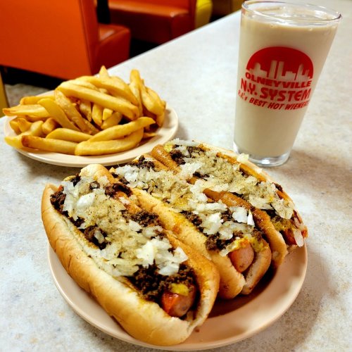 Two loaded hot dogs with onions and toppings, served with a side of fries and a milkshake in a glass.
