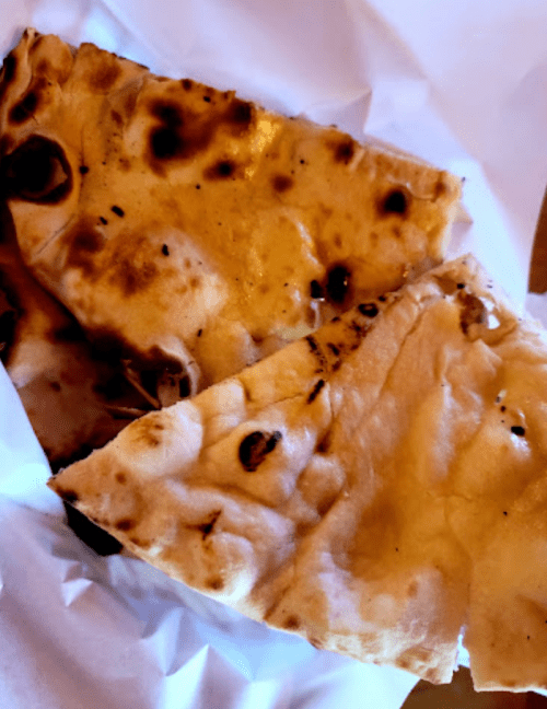 Two pieces of flatbread with charred spots, resting on white paper.