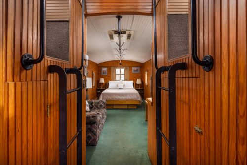 Cozy wooden interior of a bedroom with a bed, seating area, and warm lighting.